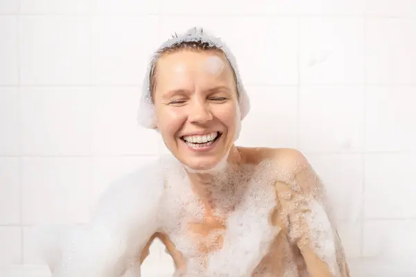 With her short haircut, a woman in her 40s smiles joyfully in her foamy bath. Serenity and bliss blend harmoniously in this relaxing moment
