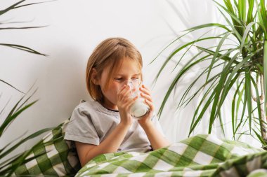 Yatakta, 9-10 yaşlarında uzun saçlı bir çocuk sütünü yudumluyor, hayal gücü rüyalarla dans ediyor, genç düşüncelere dalmış dingin bir ortam yaratıyor.