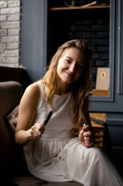 Dalgalı saçlar ve beyaz bir elbiseyle, genç bir kadın gülümsüyor, gözleri kameraya bakıyor, elinde çatal bıçak takımı var. Görüntü, onun soğukkanlı tavrını ve yemek için hazır olduğunu gösteriyor.