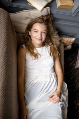 Kot pantolon ve beyaz bir bluz giymiş genç bir bayan, koltuğa yaslanmış, rahatlamanın tadını çıkarıyor.