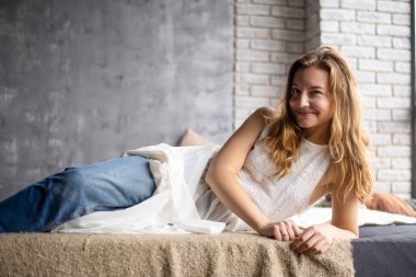 Kanepede dinlenirken, genç kadın kot pantolon ve beyaz bir bluz giyer, boş zamanlarında sükuneti kucaklar.