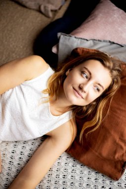 Huzurlu güzellik: beyaz gömlekli genç bir kadın, saçları özgürce süzülüyor, yumuşak bir yastıkta gevşiyor, rahatlamanın zarafetini simgeliyor.