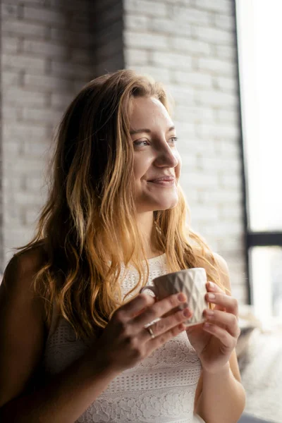 A woman\'s face is lit up by the joy of a new day, as she sips her morning coffee