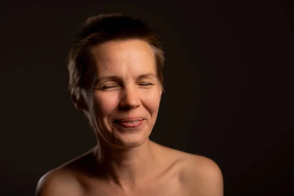 An image of self-pampering featuring a middle-aged woman with a stylish short haircut, elegantly revealing her bare shoulders, and radiating a serene smile against a sophisticated black background. Promoting skincare and self-care routines