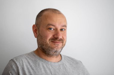 Sıradan görünümlü, tıraşsız gülümseyen ve gri arka plandaki kameraya bakan bir adam. Kırklı yaşlarda bir adam.