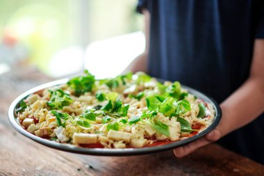 Yuvarlak şekilli çiğ pizza. Elinde bir sürü peynir ve bitkiler var..