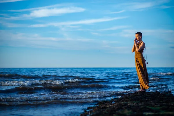 A woman prays to the setting sun on the ocean. A middle-aged woman in a long dress with a short haircut.