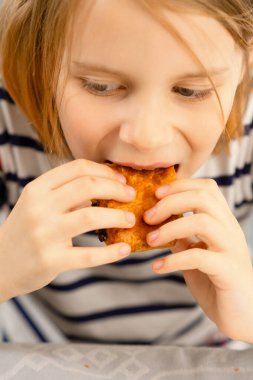 Küçük bir fırıncının zevki: Ev yapımı puf böreğin tadını çıkaran bir çocuk, her lokmada küçük bir ısırık.