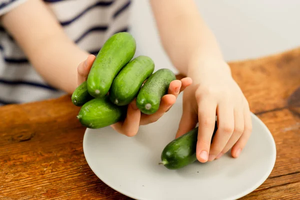Farm-to-table freshness: Child\'s hands presenting crisp green cucumbers on a wooden surface