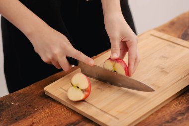 Besin zengini hazırlık: Kadının elleri tahta kesme tahtasındaki kırmızı elmayı kesiyor, sağlıklı beslenmeye olan bağlılığı, vejetaryen değerleri ve meyve tüketiminin avantajlarını simgeliyor.