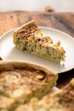 Aşçılık Sanatı: Mutfak sanatı ahşap bir masanın üstünde sergilenen yuvarlak bir pırasa ve yumurtalı tart ile açılıyor