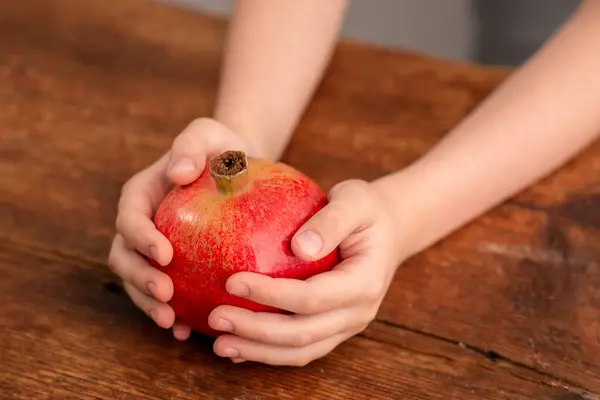 Nutrient-packed jewel: a child\'s hands reveal the beauty of a whole pomegranate, illustrating the nutritional advantages and natural elegance on a rustic wooden backdrop