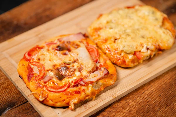 Pizza Perfection: A pair of mini pizzas featuring savory ham and melted cheese, artfully displayed on a wooden chopping block