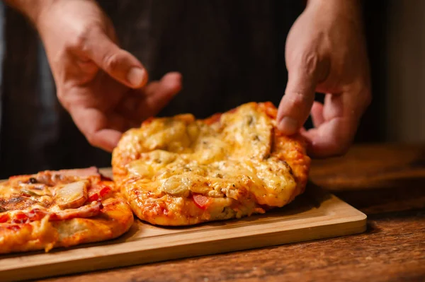 Pizza Pleasure in Hands: Male hands offer a delightful glimpse of two small homemade pizzas on a wooden surface
