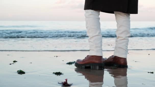 穿着靴子的女足站在大海边的湿沙滩上 波浪缓缓地逼近 用一种顽皮的触摸把靴子的脚底逗乐了 — 图库视频影像