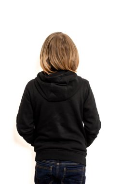 Uzun saçlı genç bir çocuk beyaz bir arka plana karşı sırtı seyirciye dönük duruyor.