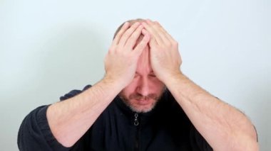 Orta yaşlı bir adam, beyaz bir arka planda elleri şokla kafasını sıktı.