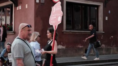 Varşova, Polonya - 20 Temmuz 2023: Bir reklam afişi tutan ve Old Town sokaklarında reklam dağıtan genç bir kadın