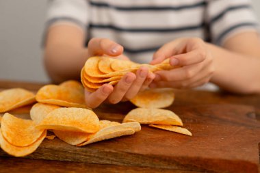 Bir çocuğun elleri patates cipsi ile meşgul, onları ahşap bir masaya istifliyor, eğlenceli bir atıştırma zamanı için..