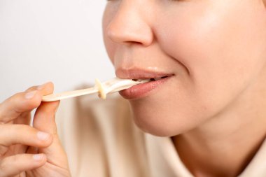 Tanımlanamayan bir kadının dondurmasını beyaz bir arka planda çubukla bitirişinin yakın çekimi. Tatlı dişli, tatlı.