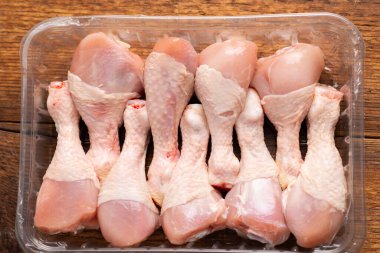 Tahta bir arka planda plastik bir kutuda taze tavuk bacağı ve bacakları. Yukarıdan görüntüle.