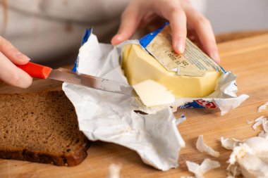Bir parça siyah ekmek üzerinde sandviç yapmak için tereyağı kesen kadın elleri..