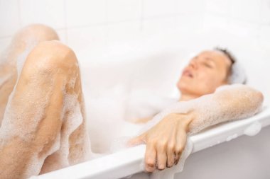 40 'lı yaşlarda, kısa saç tıraşı olan, köpük banyosunun keyfini çıkaran, mutluluk saçan bir kadın. Etrafını sükunet sarmış. Saf rahatlama ve memnuniyet..