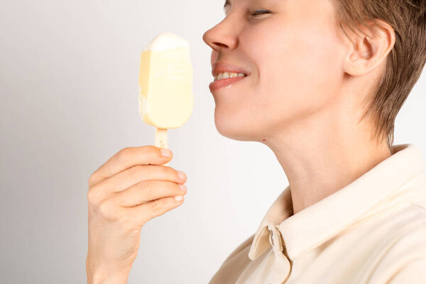 A woman in her middle years enjoys ice cream against a pristine white background, relishing the frozen delight with each delightful lick.