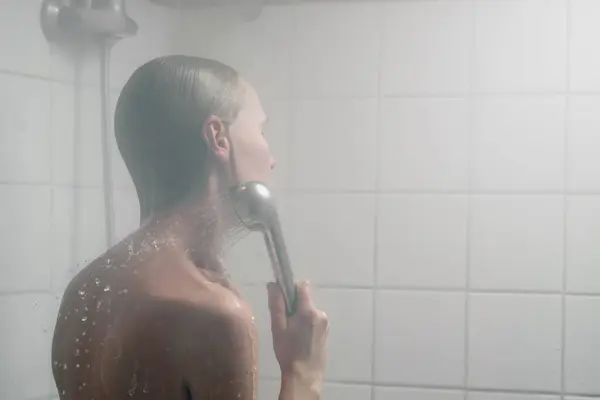 A woman at heart. Woman washing her hair in the shower in the mist of hot water.