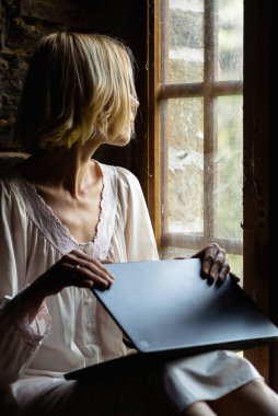 Bir kadın pencerenin yanındaki bilgisayarı kapatıyor. Mesai bitti. Serbest Çalışan, Evden Çalışan..