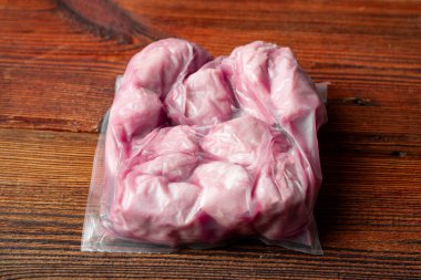 Tahta bir masanın üzerinde bir et paketi duruyor. Et plastiğe sarılı ve taze.