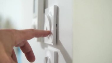 Bir insan duvardaki beyaz düğmeye dokunuyor. Düğme 