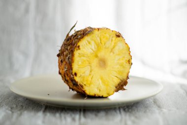 Bir dilim ananas ikiye ayrılır ve beyaz bir tabağa yerleştirilir. Tazelik ve doğal güzellik kavramı, ananasın canlı sarı rengiyle beyaz tabağın zıt olması gibi.