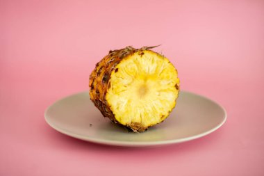 Bir dilim ananas ikiye ayrılır ve beyaz bir tabağa yerleştirilir. Ananas, tropik meyve ve tatillerin bir sembolü olduğu için, görüntünün parlak ve neşeli bir havası vardır.