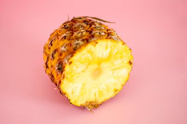 Bir dilim ananas ikiye ayrılır ve pembe arka plana yerleştirilir. Tazelik ve doğal güzellik kavramı, ananasın canlı sarı rengi pembe arka planla zıtlaşır.