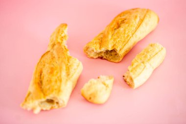 Biri ikiye bölünmüş iki parça ekmek. Diğer parça bir bütün. Ekmek pembe arka planda.