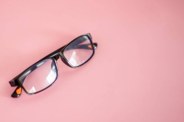 Bir çift gözlük pembe arka planda oturur. Gözlükler siyah ve mavi renkli. Odaklanma kavramı ve detaylara dikkat, çünkü ana konu gözlük ve izleyicinin gözünü çizmek.