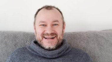 Bir adam kanepeye oturur ve ışıl ışıl gülümser, sıcaklık ve mutluluk saçar..