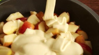 Bir kase dilimlenmiş elmanın üzerine kremalı muhallebi dökülen yakın plan bir video..