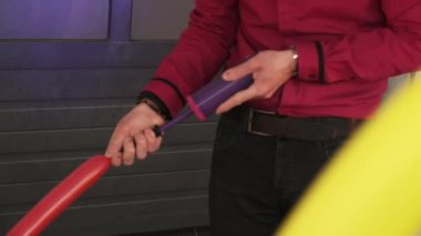 Bir balon sanatçısı mor bir pompayla uzun kırmızı bir balon şişirir..