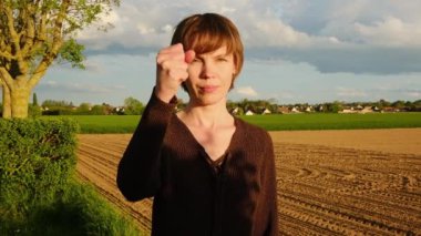 Bir kadın gün batımında bir tarlada duruyor, yemyeşil ve açık mavi gökyüzü ile çevrili..