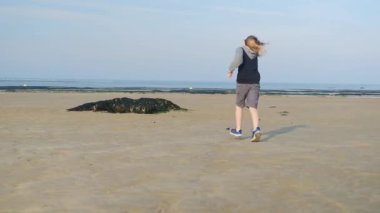 Bir insan kumlu bir sahilde yürüyor, okyanusun güzel manzarasının tadını çıkarıyor..