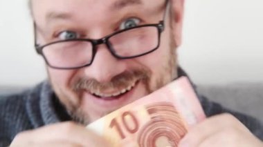 Bir adam elinde 10 avroluk banknot tutarken neşeyle gülümsüyor.