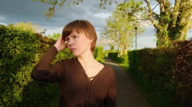 Güneşli bir günde bir kadın parkta yürüyor, altın saatin tadını çıkarıyor..