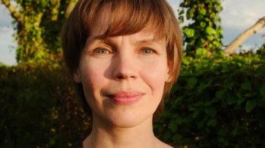 Kısa kahverengi saçlı, nazikçe gülümseyen, altın saatin sıcacık ışığında yıkanan bir kadının yakın plan portresi..