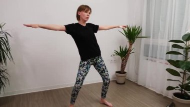 . Bir kadın, doğal ışığı olan parlak bir odada yoga akış sahnesini gerçekleştiriyor..