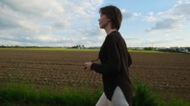 Bir kadın gün batımında tarlada koşuyor, silueti turuncu gökyüzüne karşı duruyor..