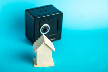 Secure savings: small wooden house and mini safe on blue background. clipart