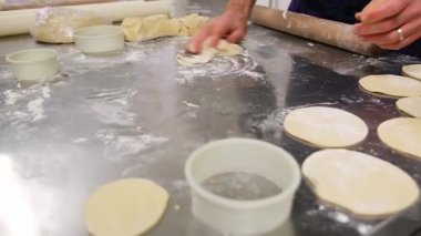 Hamur diskleri hazırlanıyor: Kurabiye keskisi ve oklavayla hamur işi yapan eller.
