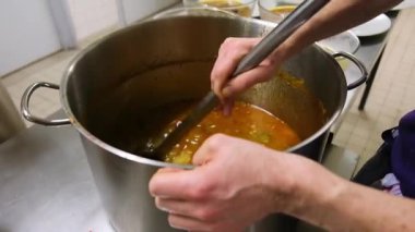 Mutfak ortamında aşçı kepçeyle sağlıklı çorbayı kâselere dolduruyor..